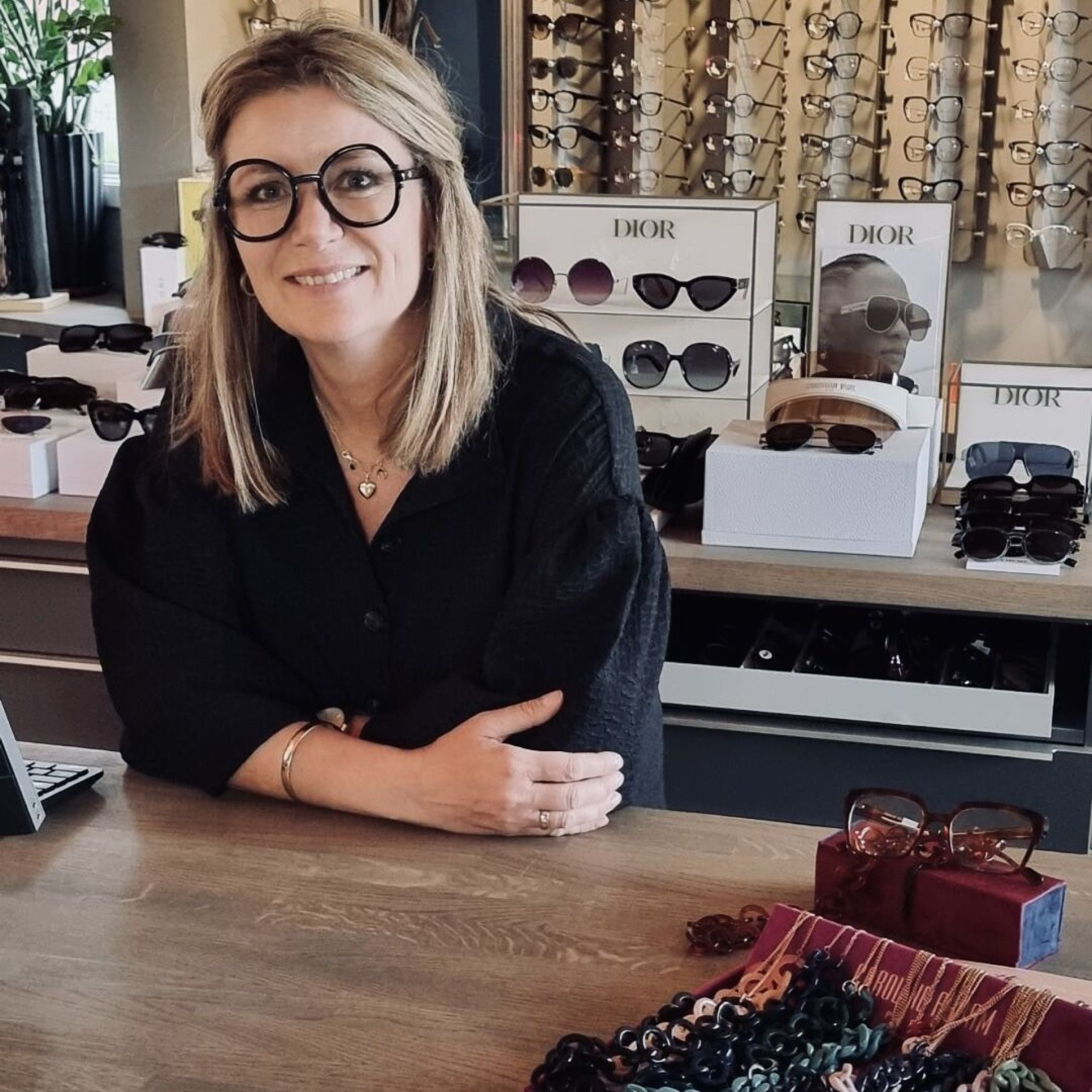 Åse Torill Årset bak disken hos Brillehjørnet med Dior-utstilling i bakgrunnen